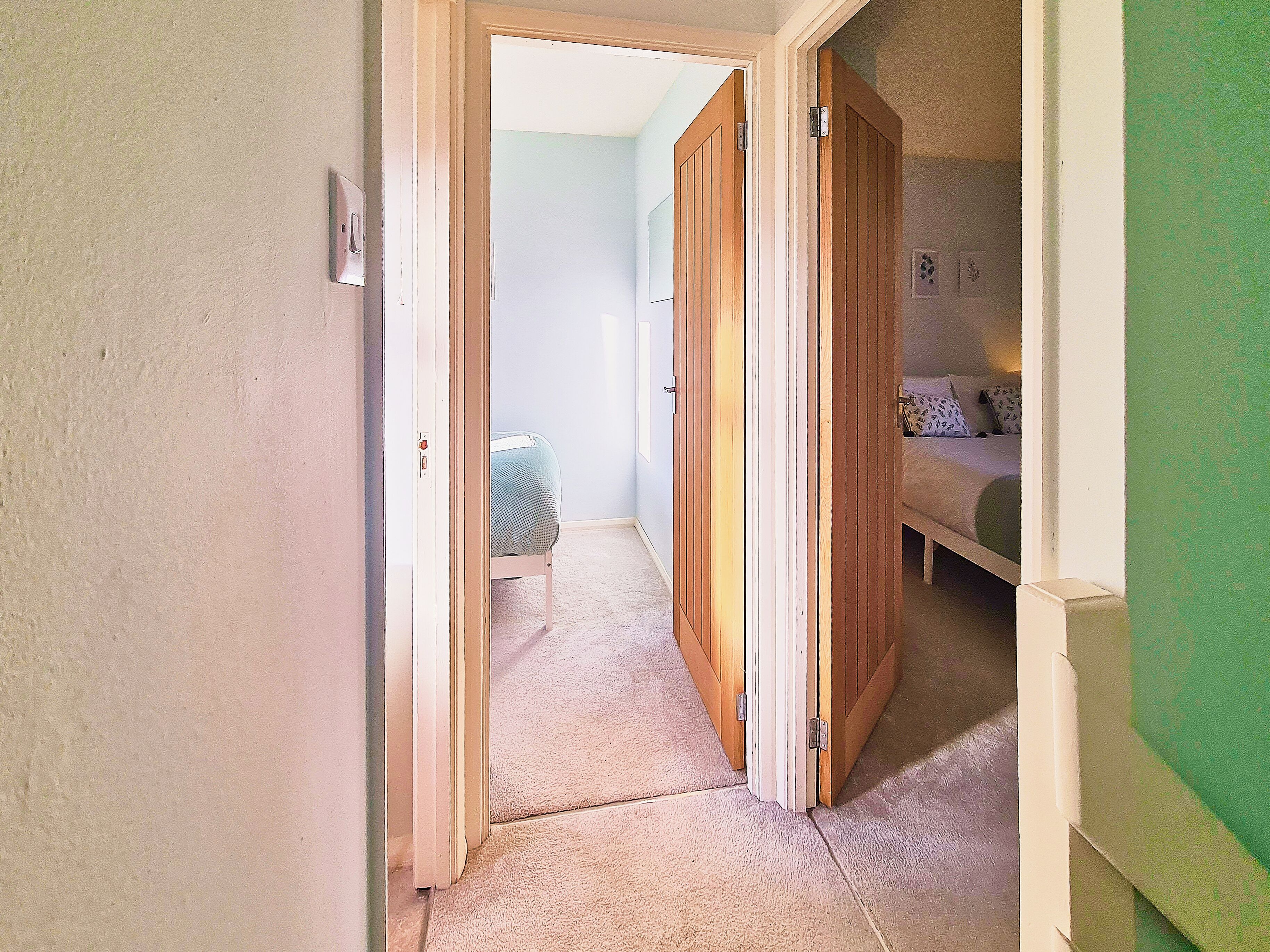 Ein schmaler Flur mit einer Tür zu einem Schlafzimmer. Der Raum verfügt über ein Bett mit einem gemusterten Überwurf und einen Nachttisch mit einer Lampe.
