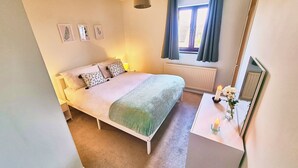 Ein Schlafzimmer mit Bett, Nachttisch, Spiegel, Fenster und Heizkörper.