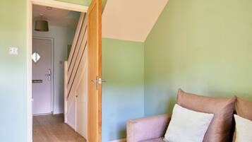 Una habitación con puerta de madera que da a una escalera, pared de color verde claro y un sofá con almohadones.