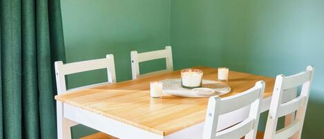 Una mesa de comedor con cuatro sillas blancas, una superficie de madera y dos velas sobre un mantel individual.