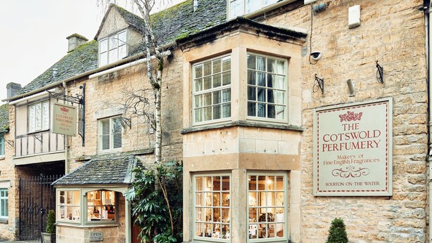 Ein traditionelles Steinhaus mit einem Schild für 'The Cotswold Perfumery', das anzeigt, dass es sich um ein Geschäft handelt.