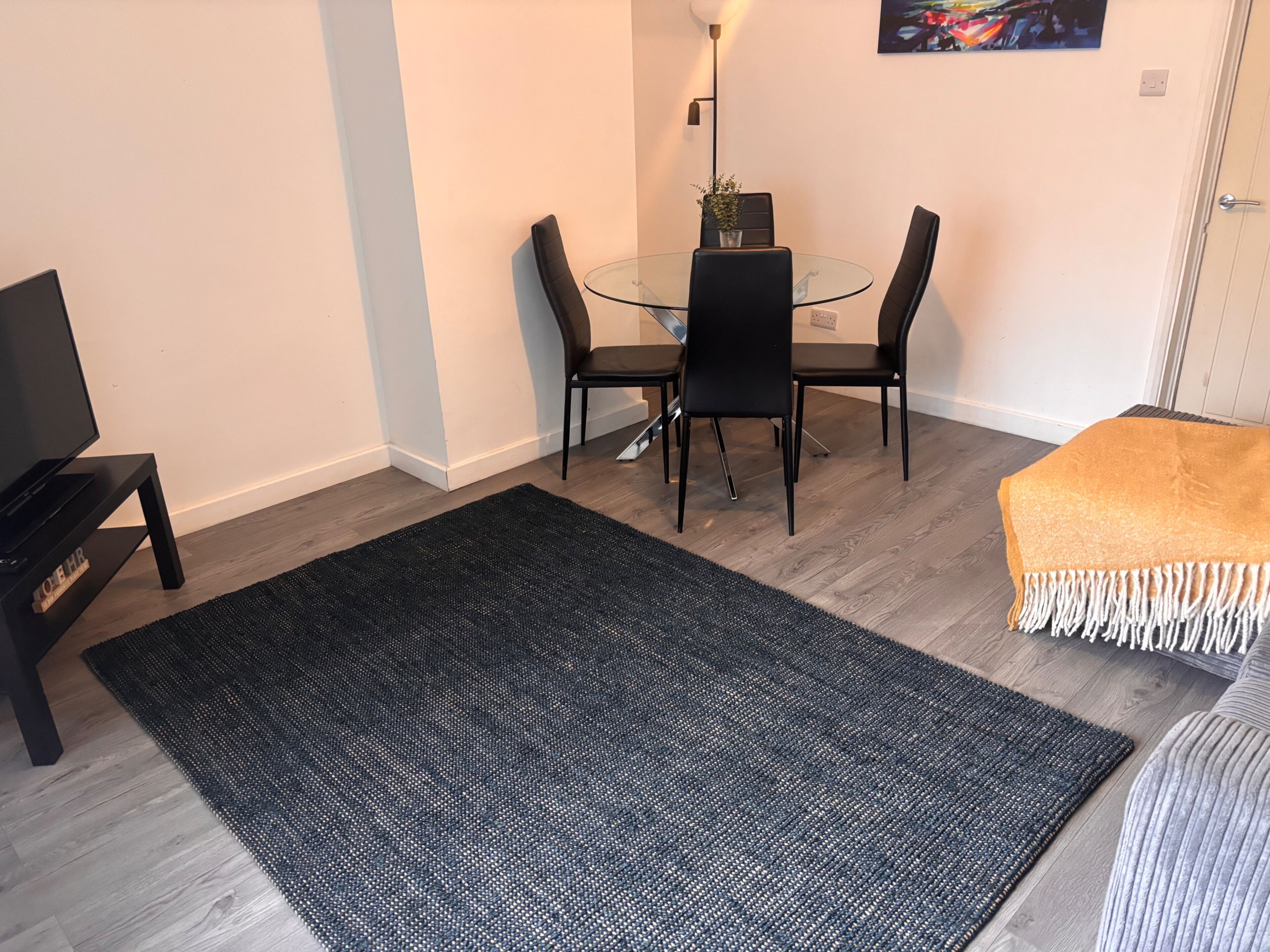 Ein Essbereich mit einem Glastisch und schwarzen Stühlen, einem schwarzen Teppich und einem beigen Sofa mit Fransen.