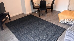 Un coin repas avec une table en verre et des chaises noires, un tapis noir et un canapé beige agrémenté d’un plaid à franges.