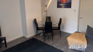Un coin repas avec une table en verre et des chaises noires, un tableau accroché au mur et une porte visible au fond.