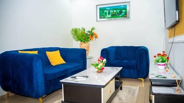 Un salón con dos sofás azules, una mesa de centro, una mesita auxiliar con flores y un cuadro en la pared.