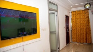 Un salón con un televisor de pantalla plana montado en una pared amarilla, un ventanal corredero y una cortina estampada.