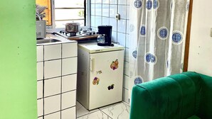 Une cuisine compacte équipée d’un réfrigérateur, d’une cuisinière et d’un évier. Une fenêtre offre une vue sur l’extérieur, et un canapé vert se trouve dans l’espace salon.