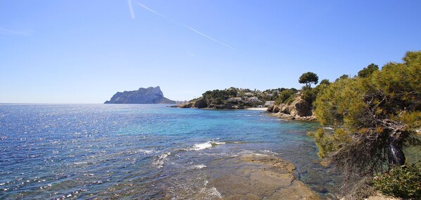 A coastal landscape with clear blue waters, rocky shores, and a distant island.