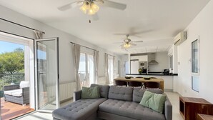 Ein modernes Wohnzimmer mit einem Ecksofa, Deckenventilatoren und einer Schiebetür zu einem Balkon.