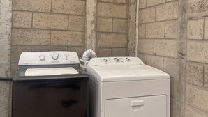Een wasserette met twee wasmachines, één zwart en één wit, tegen een bakstenen muur.