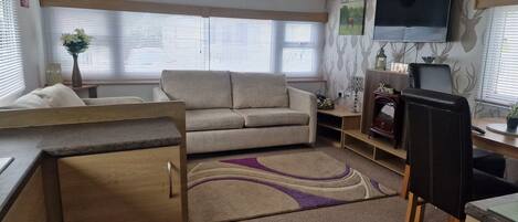 A cozy RV interior with a sofa, a dining table, a TV mounted on the wall, and a fireplace.