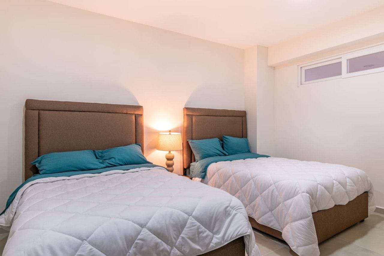 A bedroom with two beds, each with a headboard and a bedside lamp.
