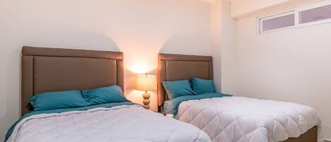 A bedroom with two beds, each with a headboard and a bedside lamp.