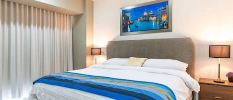 A hotel room with a bed, a nightstand, a lamp, a painting, and a window with curtains.