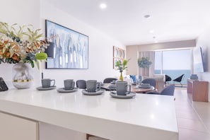 Una cocina moderna con encimera blanca, tazas grises y un florero con flores.
