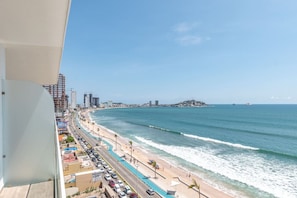 Un paisaje urbano costero con una playa, una carretera paralela a la orilla y una isla distante.