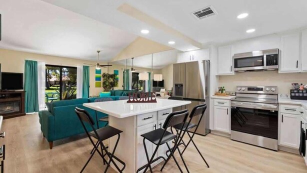 A modern kitchen with white cabinets, a central island with bar stools, a built-in oven, and a microwave. - Golf Resort 2BR | Pool, Spa & Pickleball (Palm Desert)