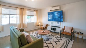 A modern living room with a sofa, chairs, a coffee table, and a TV mounted on the wall. - The Pink Agave: Retro Glam Views+Cold Plunge+Hot Tub+Gym+Dog&Festival Friendly (Yucca Valley)