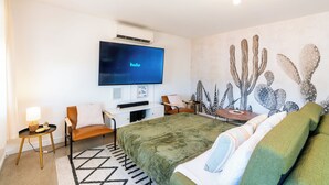 A modern hotel room with a large bed, a flat-screen TV displaying 'hulu', a cactus-themed wall, and a minimalist decor. - The Pink Agave: Retro Glam Views+Cold Plunge+Hot Tub+Gym+Dog&Festival Friendly (Yucca Valley)