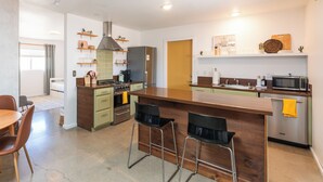 A modern kitchen with a central island, bar stools, and built-in appliances. - The Pink Agave: Retro Glam Views+Cold Plunge+Hot Tub+Gym+Dog&Festival Friendly (Yucca Valley)