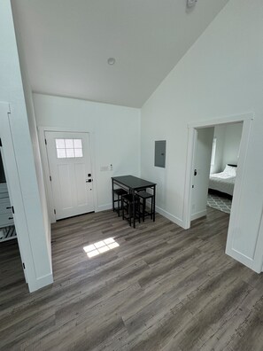 Una habitación con una mesa y sillas, una puerta, y una cama en la habitación contigua.