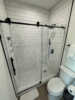 Un baño moderno con azulejos blancos tipo metro, ducha con mampara de vidrio, inodoro y toallero.