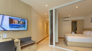A modern hotel room with a bed, a desk, and a television displaying a pool view. - Sea View Beach Dinning Beach Front c115 (Rawai)