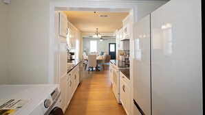 Une cuisine avec des meubles blancs, un coin repas avec une table et des chaises, et un lave-linge.