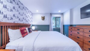 A bedroom with a wooden headboard, a large bed with white bedding, a wooden dresser, and a mounted television.