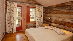 A log cabin bedroom with a wooden ceiling, a bed with a quilt, and a window with curtains. - Vacation home Naava by Interhome (Kittilä)