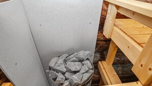 A corner of a room with a grey tiled wall, a wooden bench, and a metal container filled with rocks. - Vacation home Naava by Interhome (Kittilä)