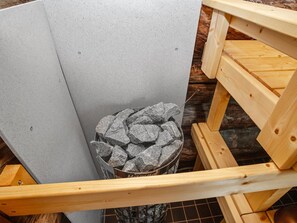 Huoneen nurkka, jossa on harmaalla laatoituksella päällystetty seinä, puinen penkki ja metallinen astia, joka on täynnä kiviä.