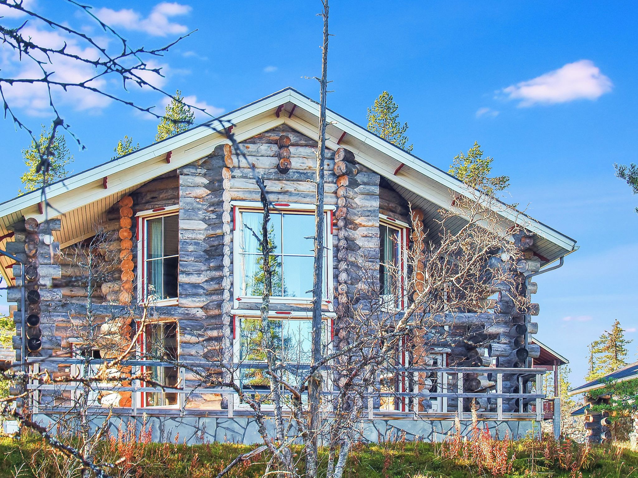 A log cabin with a stone foundation, large windows, and a porch with railings.