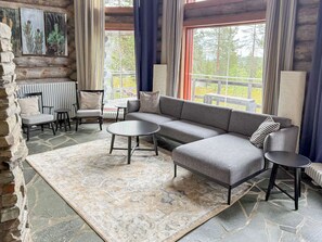 A log cabin interior with a sofa, chairs, a table, and a view of the outdoors.