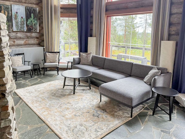 A log cabin interior with a sofa, chairs, a table, and a view of the outdoors.