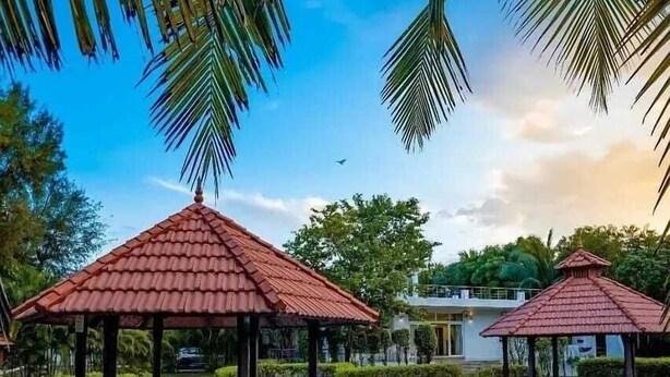 A swimming pool with a gazebo structure, surrounded by greenery and a clear sky. - Khushana Villa by Baywatch stayzz (Chennai)