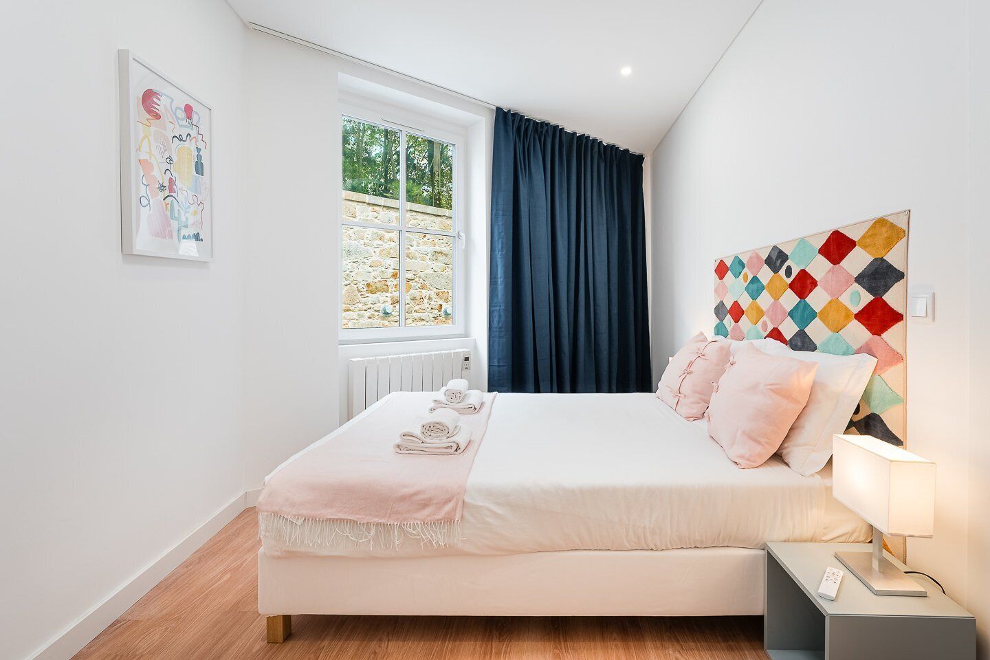 A modern bedroom with a bed, bedside table, and a window with curtains.