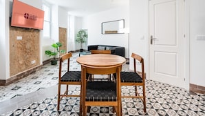 Et moderne værelse med et rundt træbord, to stole, et fjernsyn på væggen, en sofa og en potteplante.