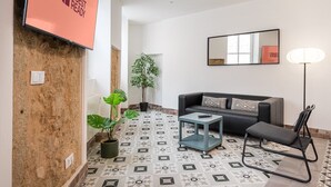 En moderne stue med sofa, sofabord, stol, potteplante og et fjernsyn der viser et logo.