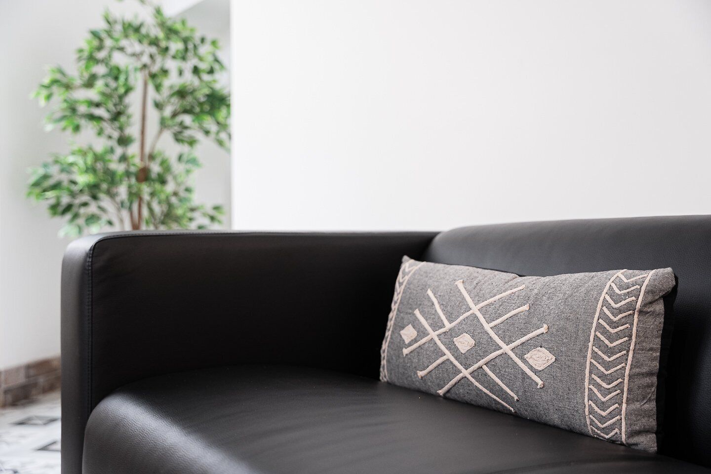 A black leather sofa with a patterned pillow.