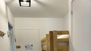 Ein schmaler Flur mit einem Stockbett, einer weißen Tür mit einem Schild und einer blauen Tür.