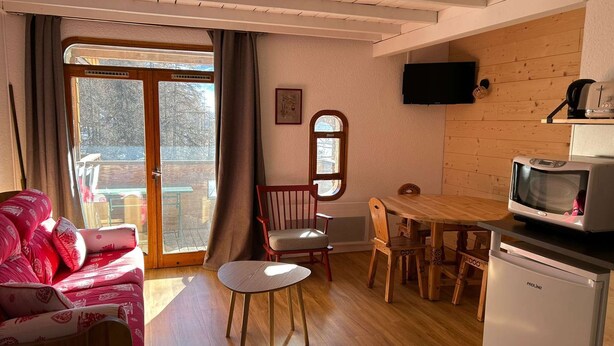 Ein gemütliches Wohnzimmer mit einer Couch, einem Esstisch mit Stühlen, einem Fernseher und einem Kühlschrank.