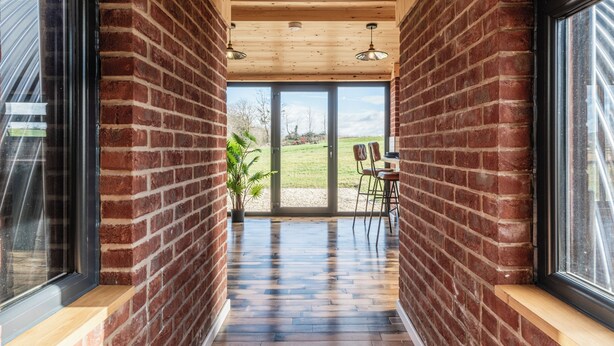 Un couloir aux murs en briques, au plancher en bois et aux grandes fenêtres.