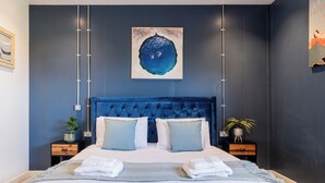 Une chambre moderne avec un grand lit, deux tables de chevet, une tête de lit bleue et une œuvre d’art accrochée au mur.