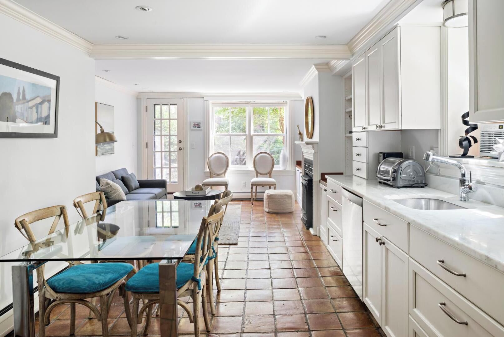A modern kitchen with white cabinetry, a dining area with a glass table, and a view through the door.