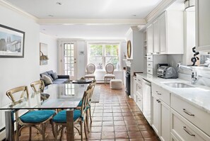 Uma cozinha moderna com armários brancos, uma área de jantar com mesa de vidro e vista pela porta.