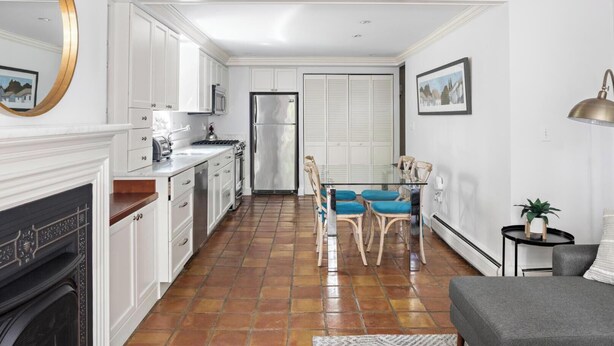 A modern kitchen with white cabinetry, a stainless steel refrigerator, and a dining area with blue upholstered chairs. - Enjoy Boston, Private Patio On Montgomery Park (Boston)