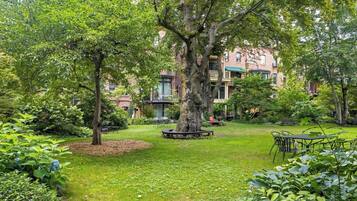 A lush garden with a large tree, a picnic table, and a building with multiple windows in the background.