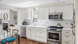 A modern kitchen with white cabinetry, stainless steel appliances, a glass dining table, and a tiled floor. - Enjoy Boston, Private Patio On Montgomery Park (Boston)