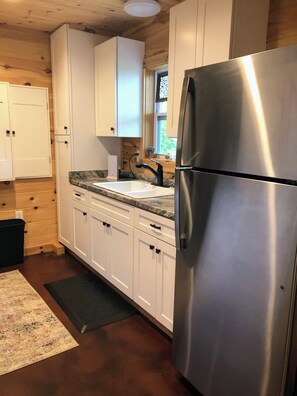 Compact kitchen with stainless steel refrigerator, white cabinetry, and granite countertop.